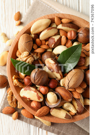 Bowl with different tasty nuts on white wooden background Bowl with different tasty nuts on white wooden background 74367096