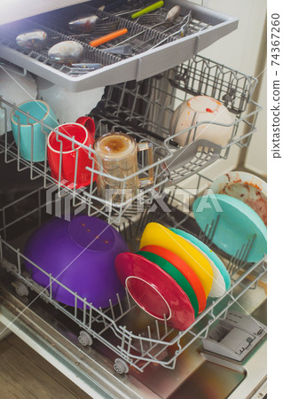Putting dirty plates in the dishwasher after dinner Putting dirty plates in the dishwasher after dinner 74367260