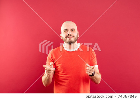 A middle-aged man with a beard in a red T-shirt on a red background stands rejoicing in victory. Isolated. 74367849