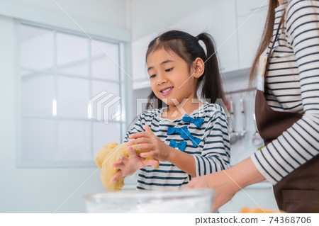 Happy Asian girl is smiling while making flour bread with her mother in home kitchen, for child activity concept. Happy Asian girl is smiling while making flour bread with her mother in home kitchen, for child activity concept. 74368706