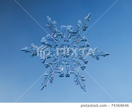 Snowflake on smooth gradient background. Macro photo of real snow crystal on glass surface. This is small snowflake with unusual pattern. 74369646