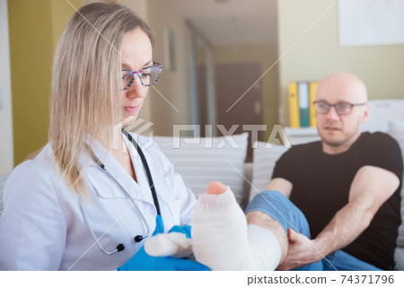 The patient after the accident.Professional nurse bandages a patient's leg with a medical bandage. The patient after the accident.Professional nurse bandages a patient's leg with a medical bandage. 74371796