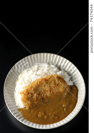 A black background shot of a cutlet curry with a large pork cutlet in the middle (overhead view) 74374044