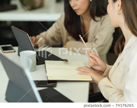 Two businesswomen brainstorming on their work while meeting in office room Two businesswomen brainstorming on their work while meeting in office room 74376265