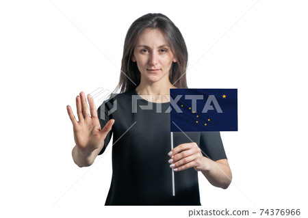 Happy young white woman holding flag of Alaska and with a serious face shows a hand stop sign isolated on a white background 74376966