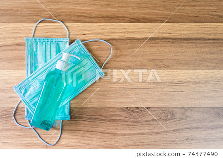 Blue Protective disposable medical mask and alcohol hand sanitizer on wooden background,Top view office table,Concept of Prevention of the spread of COVID-19 virus infection Blue Protective disposable medical mask and alcohol hand sanitizer on wooden background,Top view office table,Concept of Prevention of the spread of COVID-19 virus infection 74377490