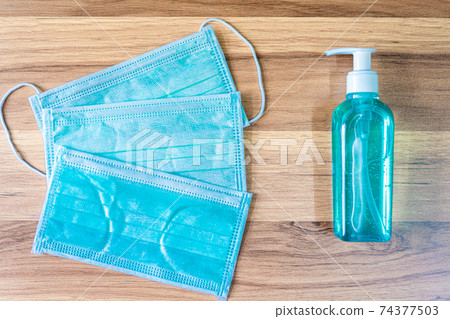 Blue Protective disposable medical mask and alcohol hand sanitizer on wooden background,Top view office table,Concept of Prevention of the spread of COVID-19 virus infection Blue Protective disposable medical mask and alcohol hand sanitizer on wooden background,Top view office table,Concept of Prevention of the spread of COVID-19 virus infection 74377503