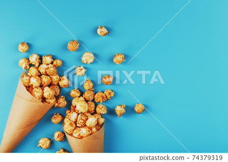 Popcorn in caramel glaze in a paper envelope on a blue background. 74379319