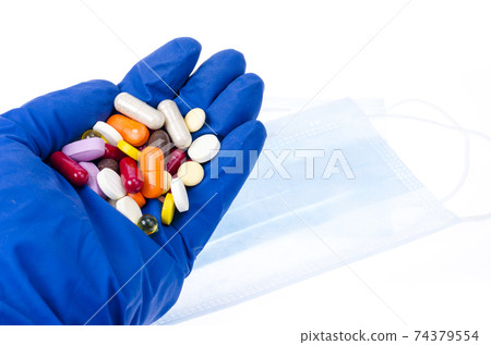 Hand in medical glove holds colored pills, pills and capsules. 74379554