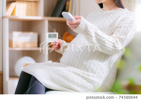 看著溫濕度計並通過遙控器操作的孕婦 看著溫濕度計並通過遙控器操作的孕婦 74380694