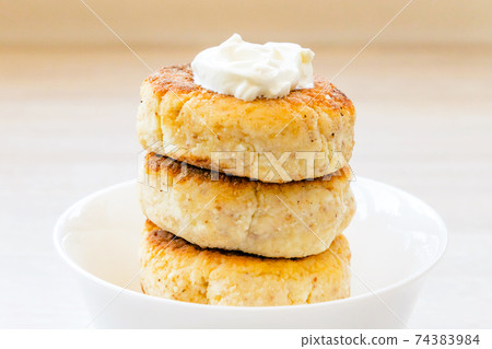 Homemade cottage cheese pancakes syrniki stack on round white bowl on white rustic table background Homemade cottage cheese pancakes syrniki stack on round white bowl on white rustic table background 74383984