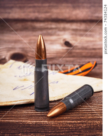 two cartridges, bullet casings on a wooden background, letters about the war the St. George ribbon as a symbol of the Second World War for Victory Day on May 9 two cartridges, bullet casings on a wooden background, letters about the war the St. George ribbon as a symbol of the Second World War for Victory Day on May 9 74384124