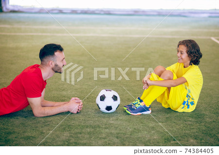 Boy in yellow uniform resting after the game and talking to his coach Boy in yellow uniform resting after the game and talking to his coach 74384405