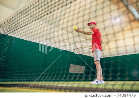 Young bearded man in a red cap ready to hit the tennis ball 74384479