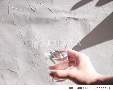 拿著透明杯水的手。加水並喝水。 拿著透明杯水的手。加水並喝水。 74385324