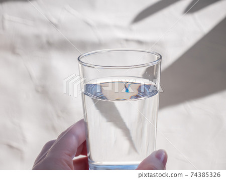 拿著透明杯水的手。加水並喝水。 拿著透明杯水的手。加水並喝水。 74385326