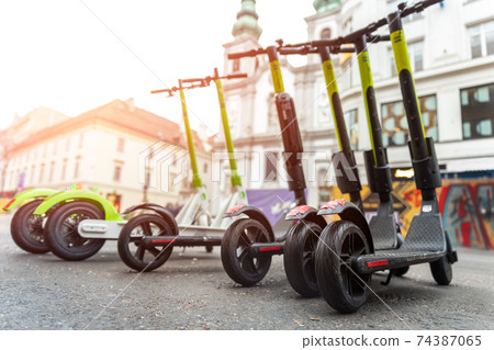 Many modern electric kick scooters sharing parked on city street. Self-service stree transport rental service. Rent urban mobility vehicle with smartphone application. Zero emission green eco energy. Many modern electric kick scooters sharing parked on city street. Self-service stree transport rental service. Rent urban mobility vehicle with smartphone application. Zero emission green eco energy. 74387065