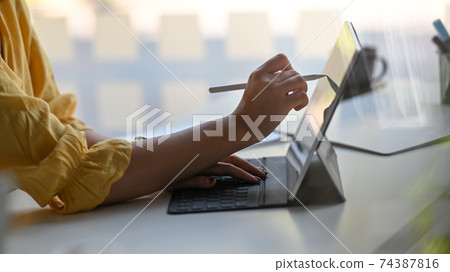 Cropped image of Designer woman's hand using a stylus pen to drawing on computer tablet with keyboard case that putting on white working table over comfortable office as background. 74387816