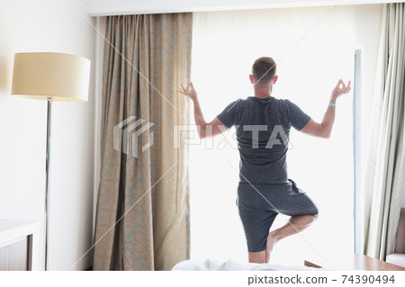 Man stands in lotus position by window 74390494