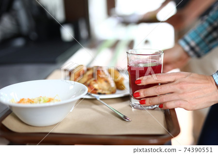 On tray are plates with dinner dishes, female hand holds glass of red liquid 74390551
