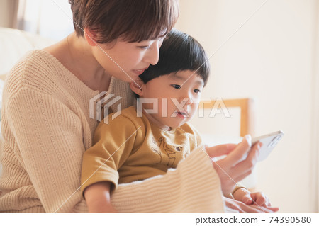 Young mother looking at a boy and a smartphone at home Young mother looking at a boy and a smartphone at home 74390580