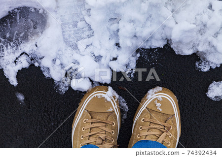 Women's feet in sneakers and jeans on a snowy track. Women's feet in sneakers and jeans on a snowy track. 74392434