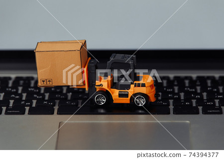 Orange forklift model and carton box on a keyboard. Courier service concept Orange forklift model and carton box on a keyboard. Courier service concept 74394377