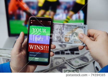 Smartphone with betting mobile application and laptop with online football broadcast behind. Bet wins Smartphone with betting mobile application and laptop with online football broadcast behind. Bet wins 74394385