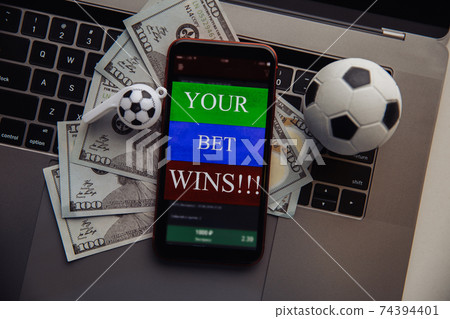 Smartphone with online gambling application, dollar bills and soccer ball on a keyboard. Betting concept. Top view Smartphone with online gambling application, dollar bills and soccer ball on a keyboard. Betting concept. Top view 74394401