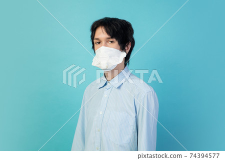 Man in protective face mask isolated on blue studio background. New rules of COVID spreading prevention 74394577