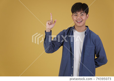 portrait of happy young asian man dressed casually pointing finger up at copyspace. yellow background portrait of happy young asian man dressed casually pointing finger up at copyspace. yellow background 74395073