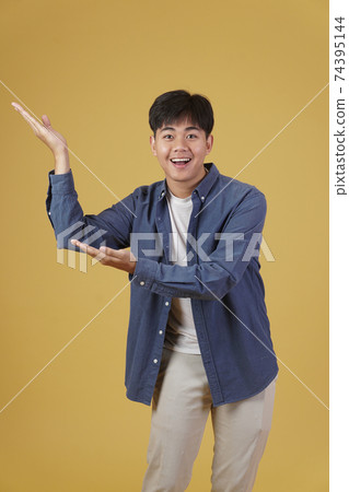 portrait of happy handsome young asian man dressed casually presenting with open palms gesture at copyspace. yellow background 74395144