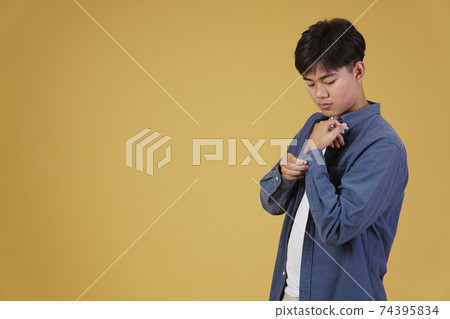 portrait of handsome young asian man in casual clothing buttoning sleeves shirt cuff. yellow background 74395834