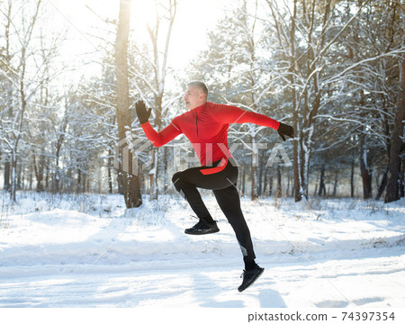 Full length portrait of strong mature sportsman jogging outside in sunny winter park. Seasonal sports and activities 74397354
