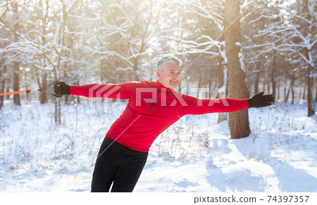 Outdoor functional strength training. Senior athletic man stretching arm muscles with resistance straps at snowy park Outdoor functional strength training. Senior athletic man stretching arm muscles with resistance straps at snowy park 74397357