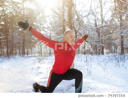 Futness suspension training concept. Athletic senior man working out with sports equipment on snowy winter day at park 74397359