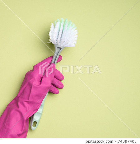 female hand in purple rubber gloves holds a plastic cleaning brush on green background female hand in purple rubber gloves holds a plastic cleaning brush on green background 74397403
