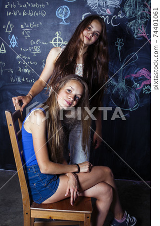 back to school after summer vacations, two teen real girls in classroom with blackboard painted together, lifestyle people concept 74401061