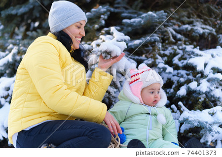 family portrait in the winter forest, mother and baby sitting and playing with snow, beautiful nature with snowy fir trees family portrait in the winter forest, mother and baby sitting and playing with snow, beautiful nature with snowy fir trees 74401373