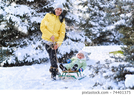 mother and child walks in the winter forest, mom rides a baby on a sled, bright snowy fir trees, beautiful nature mother and child walks in the winter forest, mom rides a baby on a sled, bright snowy fir trees, beautiful nature 74401375