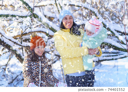family throwing snow in the winter forest, mother and children, bright sunlight and shadows on the snow, beautiful nature 74401552