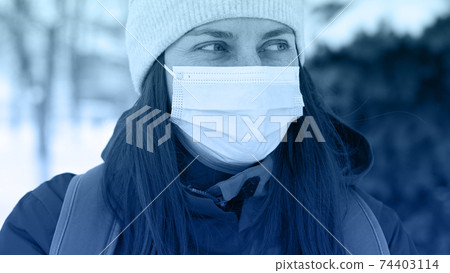 Young Caucasian woman wearing medical mask at street of city in winter time. Safety in public place during coronavirus outbreak. 74403114