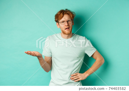 Confused redhead man trying to understand something, squinting clueless and stretch out one hand, looking puzzled, standing over mint background Confused redhead man trying to understand something, squinting clueless and stretch out one hand, looking puzzled, standing over mint background 74403582