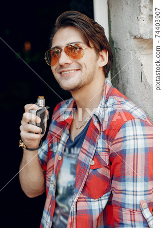 Stylish and elegant man in a city with vape 74403907