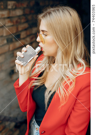 Stylish young girl in a city with vape 74403965