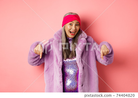 Fashion and shopping concept. Excited asian elderly woman checking out special deal, pointing fingers down and smiling happy at camera, showing advertisement, pink background Fashion and shopping concept. Excited asian elderly woman checking out special deal, pointing fingers down and smiling happy at camera, showing advertisement, pink background 74404820