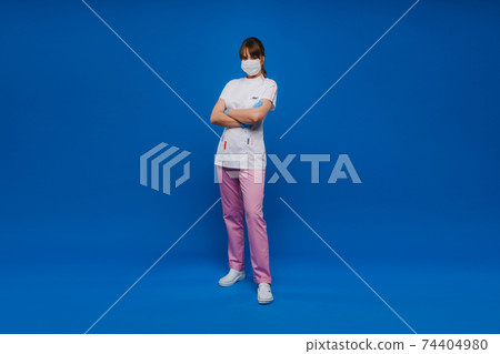 A female doctor stands in a medical mask, isolated on a blue background.A nurse in white clothes on a blue background A female doctor stands in a medical mask, isolated on a blue background.A nurse in white clothes on a blue background 74404980
