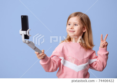 Little girl blogger influencer records videos from the blog on a smartphone, communicates with subscribers, puts likes, takes selfies,, remote learning on an isolated background. 74406422