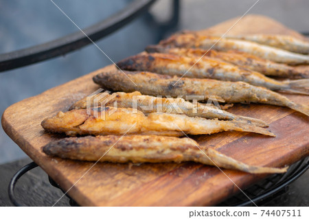Crispy breaded european smelt fish on wooden cutting board at food festival Crispy breaded european smelt fish on wooden cutting board at food festival 74407511