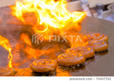 Process of grilling fresh spiral pork sausages on brazier with hot flame Process of grilling fresh spiral pork sausages on brazier with hot flame 74407592